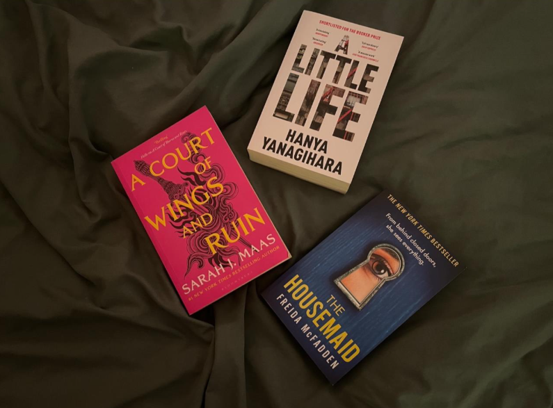 image of three books, white, pink and blue, on a dark sheet taken from directly above.