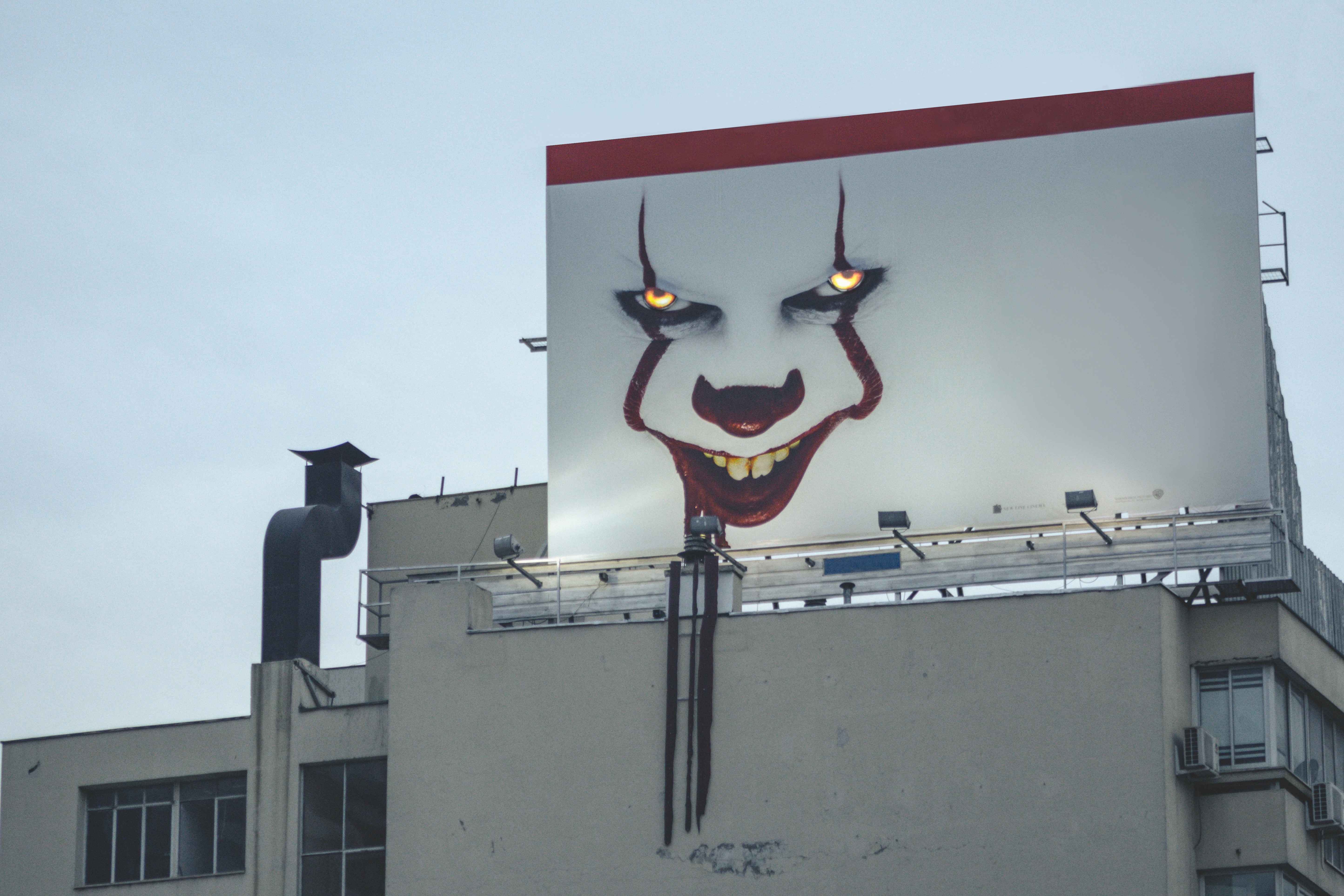 Image of a creepy clown painting on an industrial building, clear sky behind.