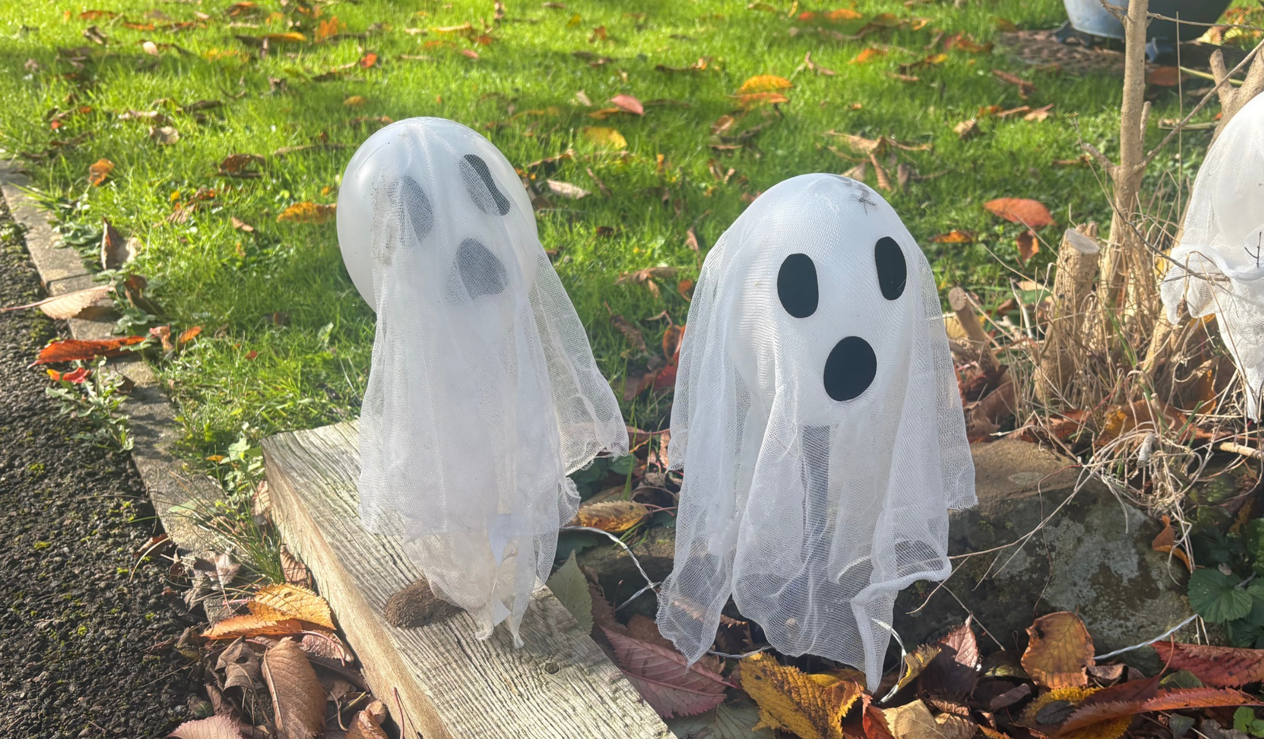 Two little ghost decorations on sticks in an autumn garden